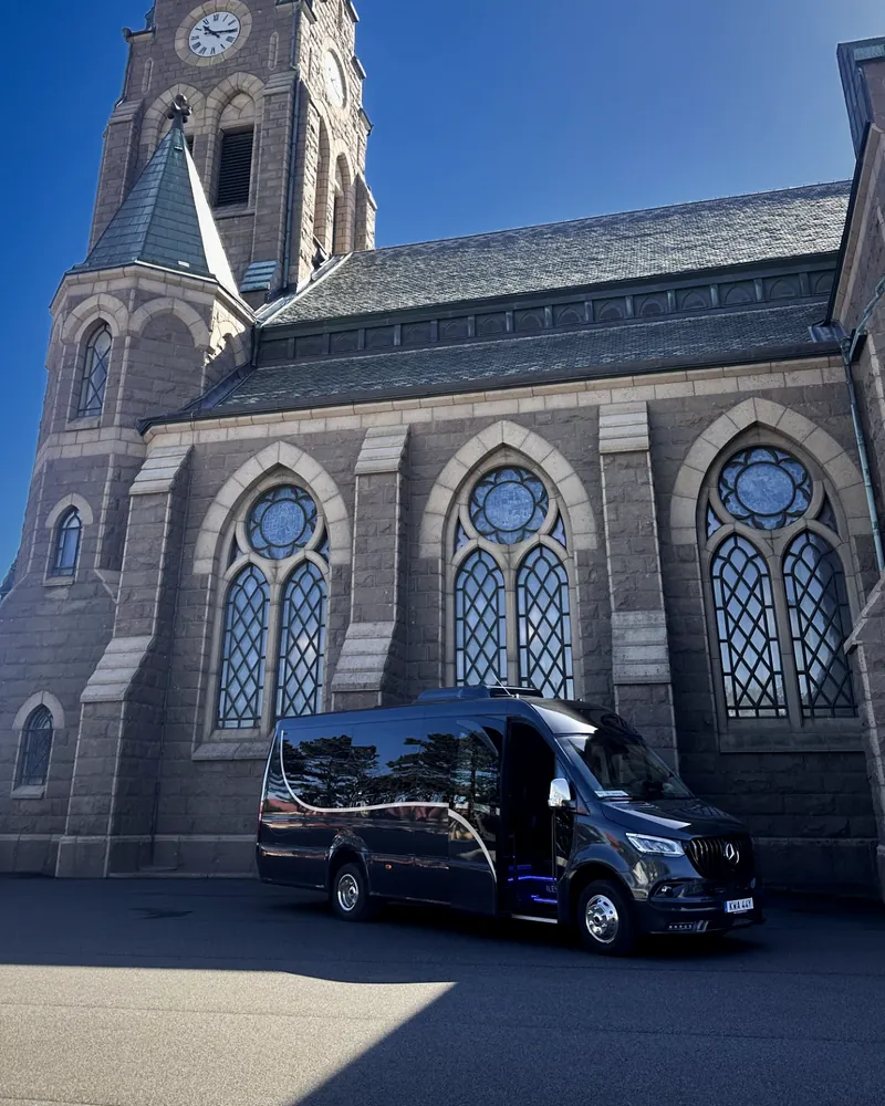 En stenkyrka med Öckeröbussarnas svarta Mercedes Sprinter parkerad framför.