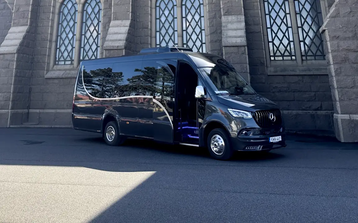 Öckeröbussarnas VIP-buss, en svart Mercedes Sprinter med öppen passagerardörr, framför en stenkyrka.