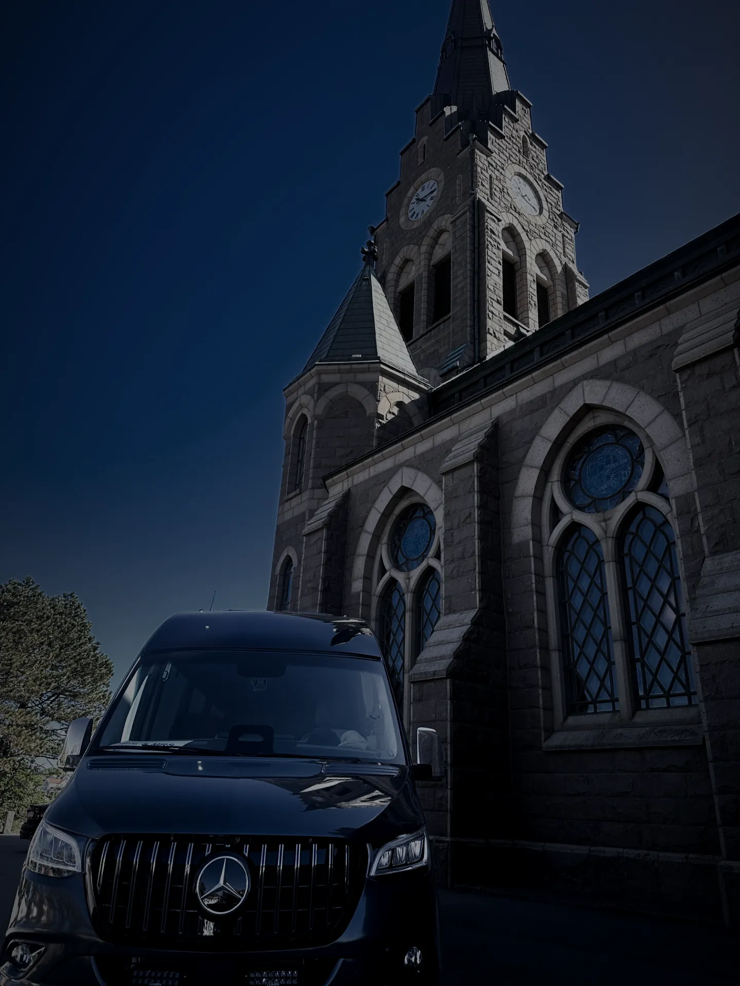Öckeröbussarnas svarta Mercedes Sprinter framifrån, med Mercedes-emblemet och en stenkyrka i bakgrunden.